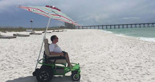 Man in a wheelchair with an umbrella at the beach